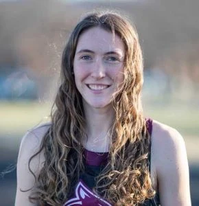 This image depicts a girl in a track uniform smiling at the camera. 