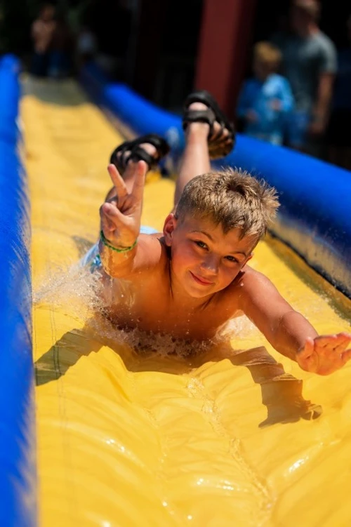 A child is sliding down a water slide while holding a peace sign. 