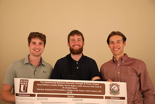 three men smiling holding a poster board
