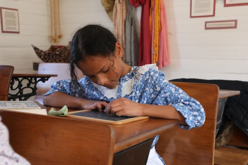 Second grader writes on slate at desk. 