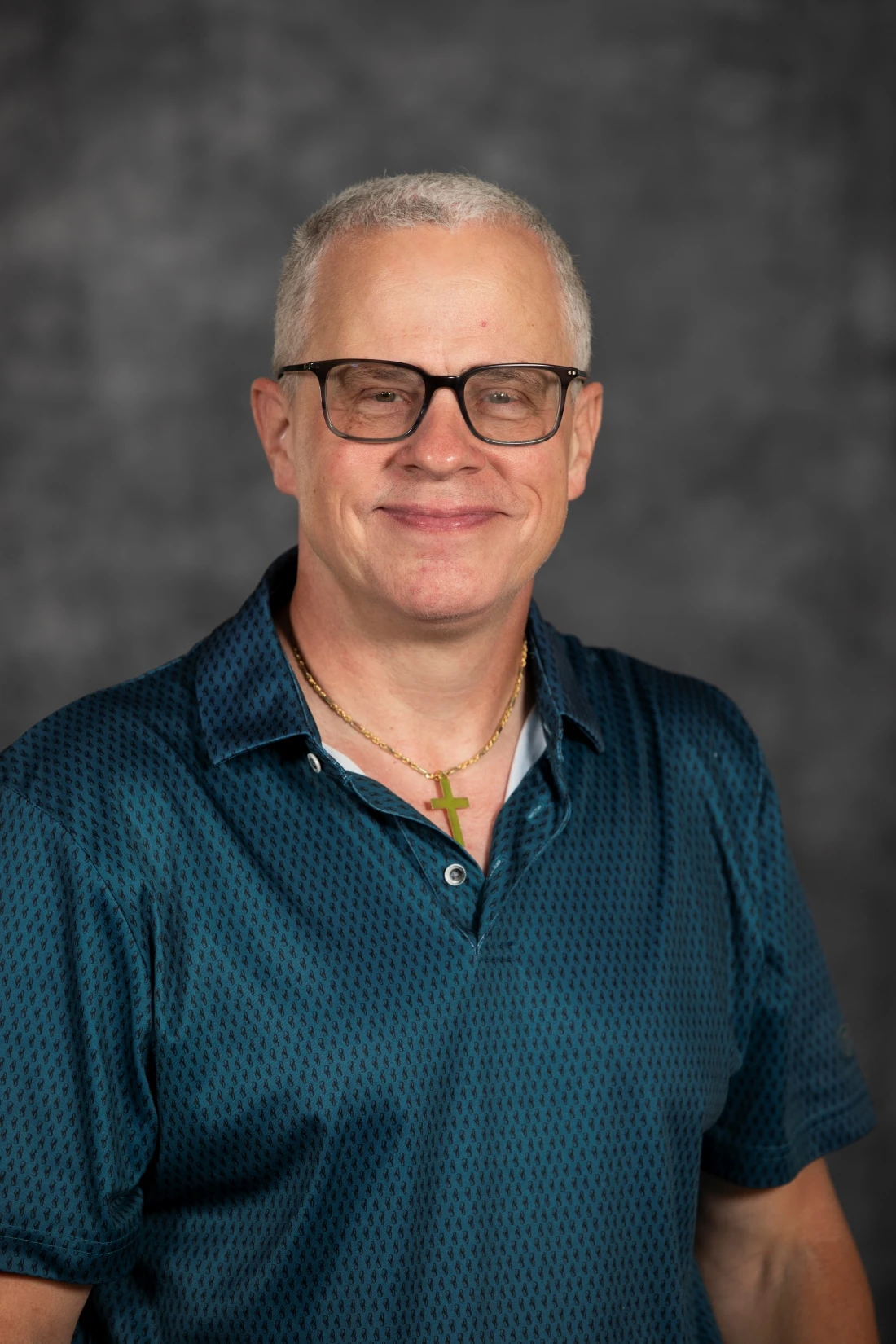 This image depicts a man smiling in front of a grey background. 