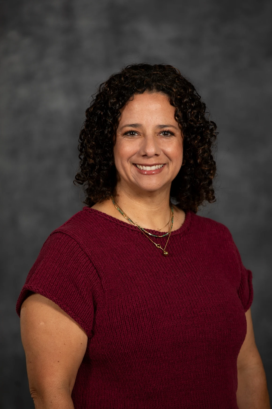 This image depicts a woman smiling in front of a grew background. 