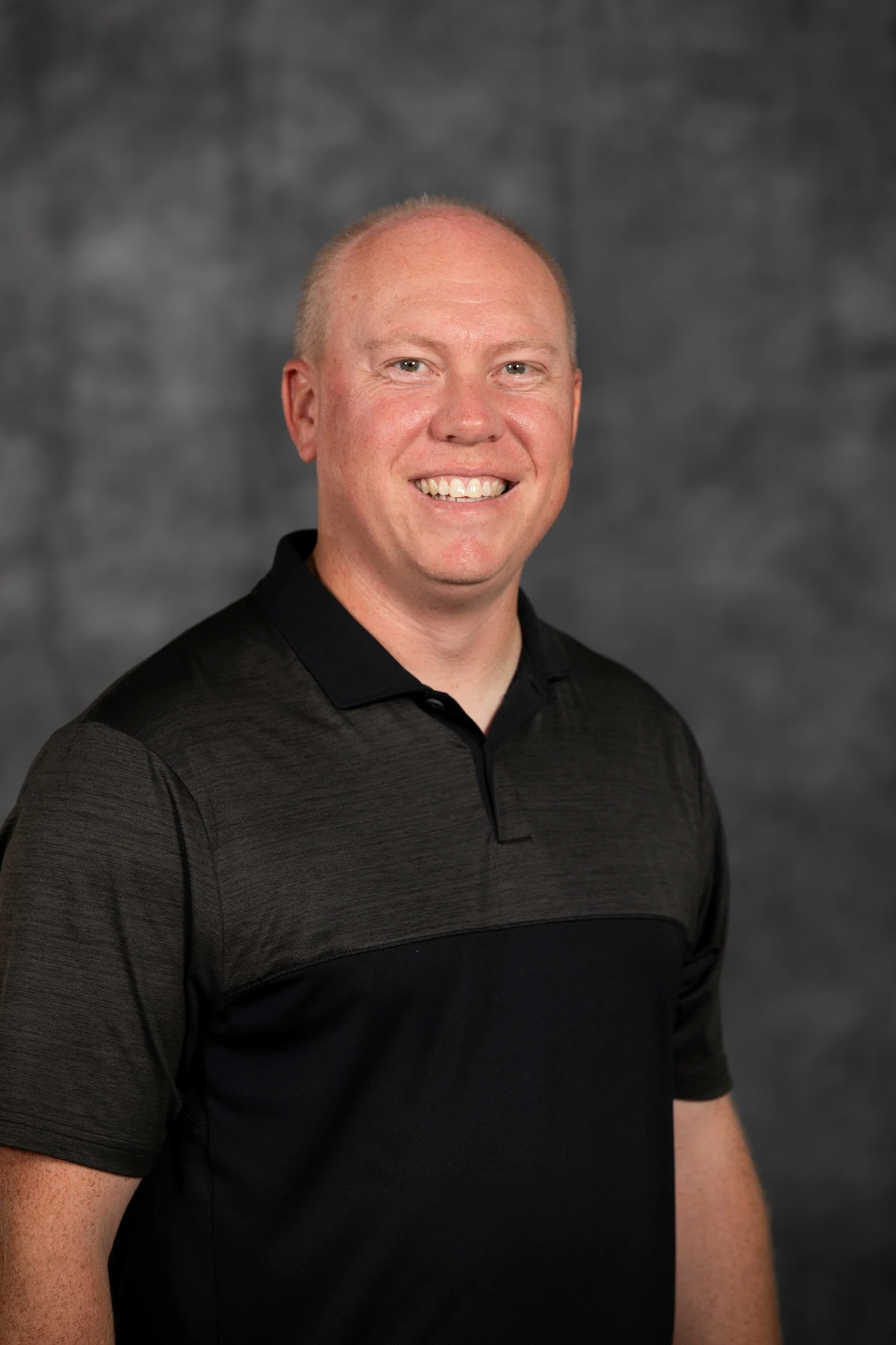 This image depicts a man smiling in front of a grey background.