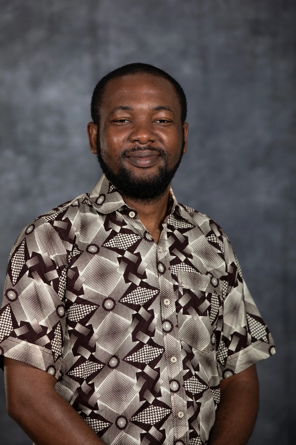 This image depicts a man smiling in front of a grey background. 