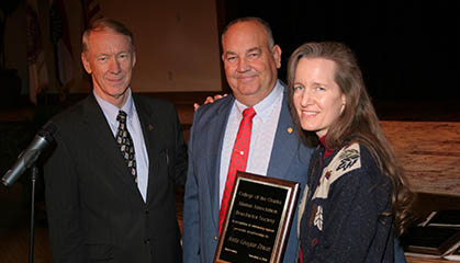 Three people holding a plaque infront of a microphone.