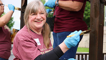 A lady painting wood while staring directly at the camera.